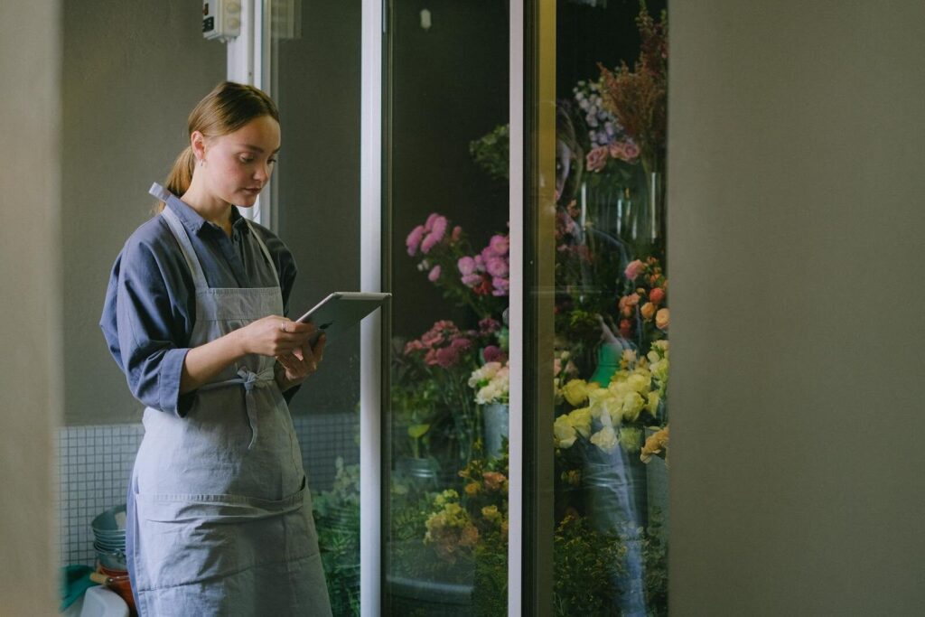 Florist in apron using digital tablet beside flower display indoors.