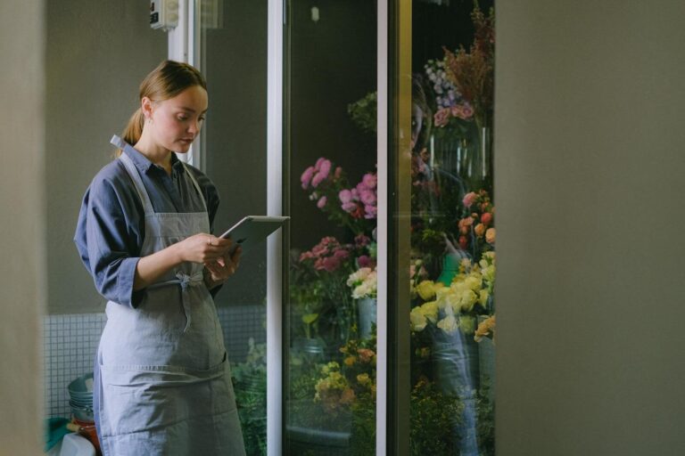 Florist in apron using digital tablet beside flower display indoors.